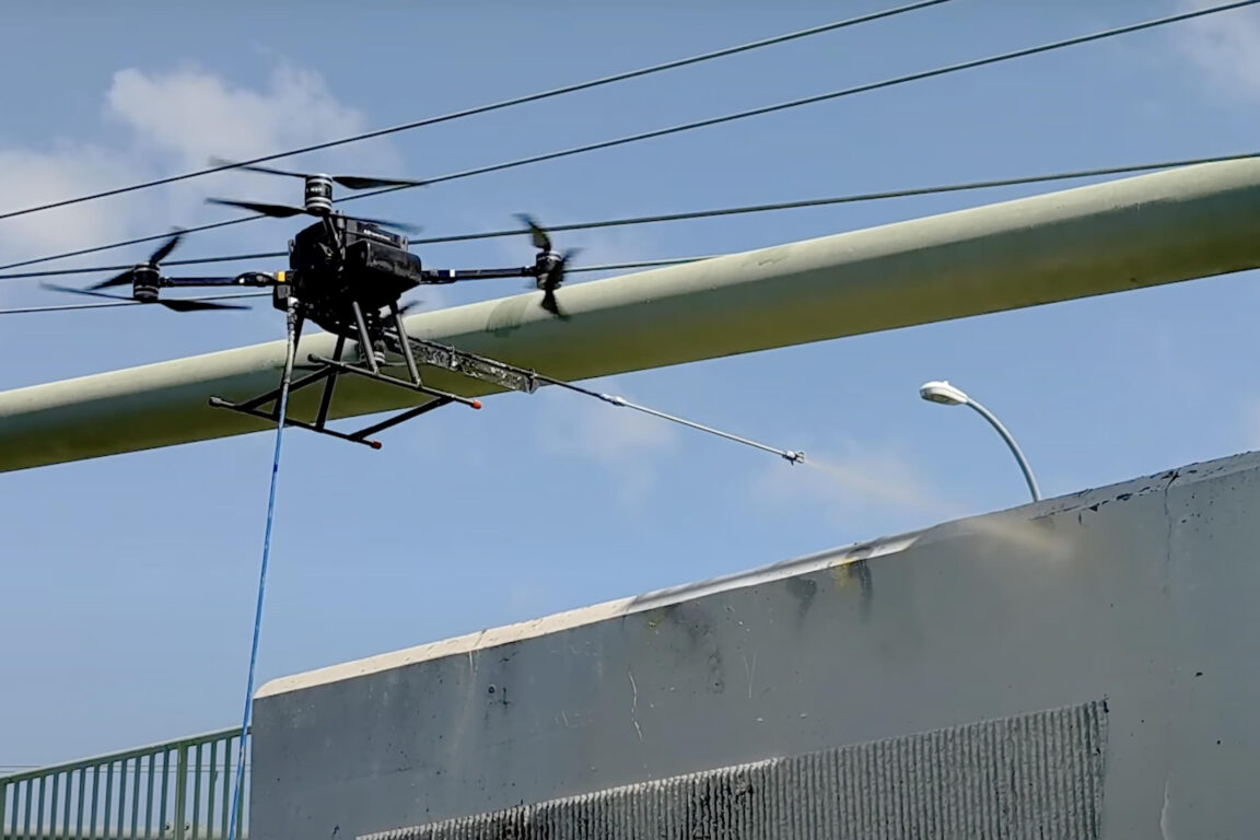 Un drone Aqualine Endure spruzza vernice grigia su un muro.